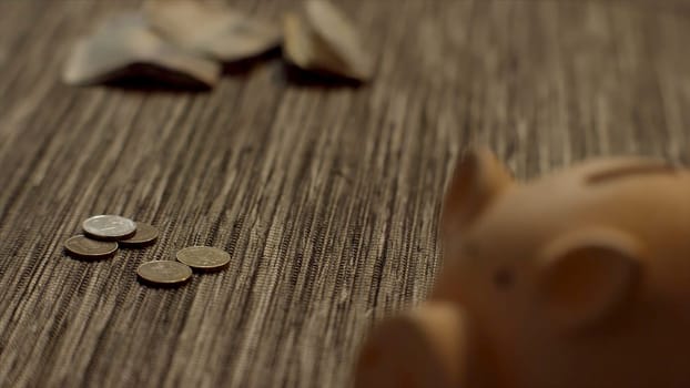Close up for piggy bank with coins falling on the old wooden table, saving money concept. Pink moneybox with many coins falling and lying on the table.