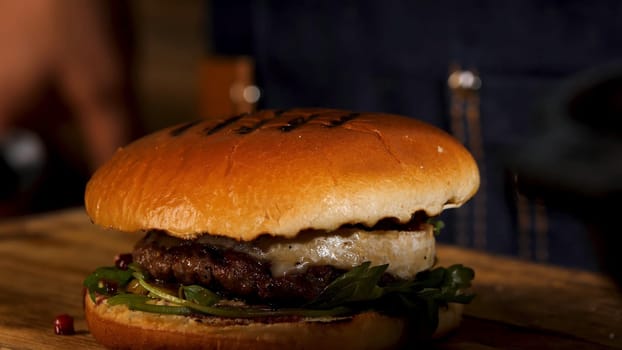 Close up of home made tasty burger on wooden table, gastronomy and foodporn concept. Stock footage. Juicy sandwich with beef, cheese, lettuce and onion.