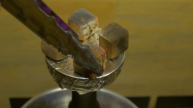 Man's hand puts burning coals on clay bowl with tobacco for hookah, Hookah's head. Hookah topic: Bartender holding a forceps with coal for hookah and puts them into a clay bowl