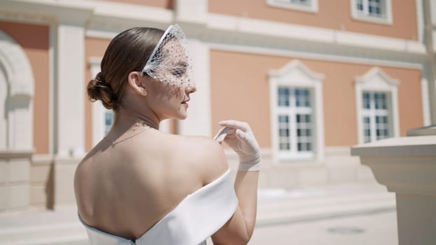 A portrait of a happy beautiful brunette bride with a veil on her face. Action. White dress with an open back on a young and elegant woman