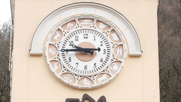 Close up of old tower of beige color with white clock dial surrounded by signs of zodiac. Stock footage. Architectural details of old clock tower.