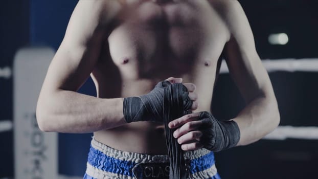 Closeup of a mixed martial arts fighter wrapping his hands before a fight. Boxer wraps his hand a red bandage before the figh