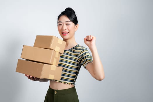 Young woman holding boxes celebrating victory and success very excited with raised arms