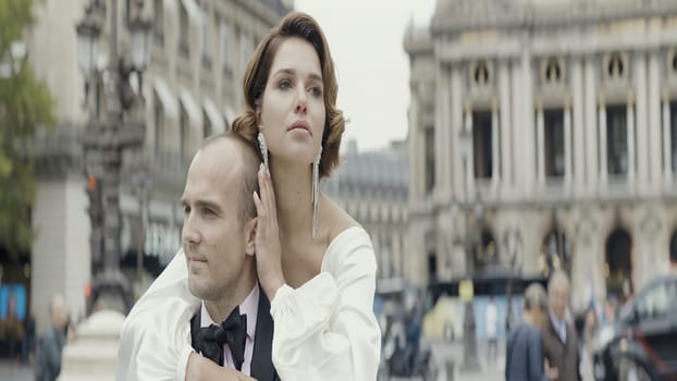 A man picks up his wife in his arms. Action. A date on the street where a girl in a white dress with a beautiful styling who jumps on her hands on a man in a suit in the fresh air.
