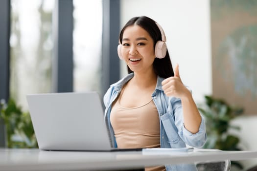 Happy asian female student recommending online studying course, showing thumb up and smiling at camera