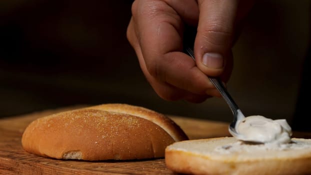 Preparing delicious burgers process, close up of male chef putting white mayonnaise sauce on a hamburger bun. Stock footage. Gastronomy concept.