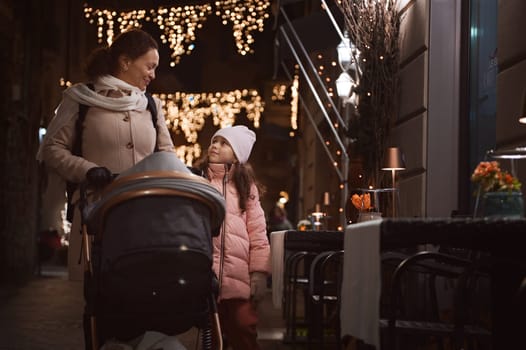 Happy mother and daughter strolling the street together, enjoying the walk in the night time during Christmas funfair
