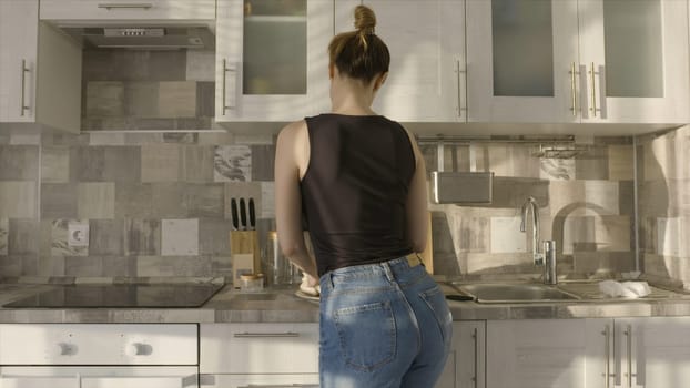 Attractive woman cooks chicken. Action. Sexy woman dancing marinating chicken in home kitchen. Beautiful woman cooks with passion at home