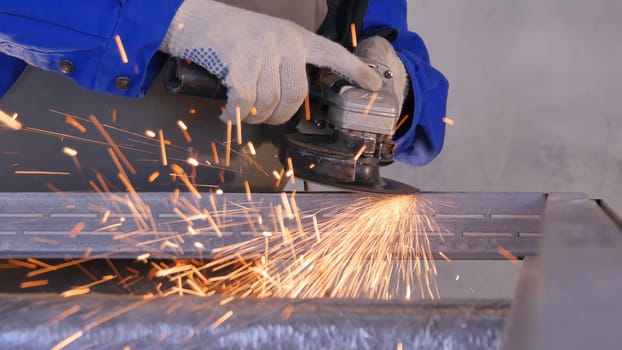 Craftsman sawing metal with disk grinder in workshop. Grinding metal with sparks flying. Electric wheel grinding on steel structure in factory Low speed shutter. Metal grinding with orange flying sparks.