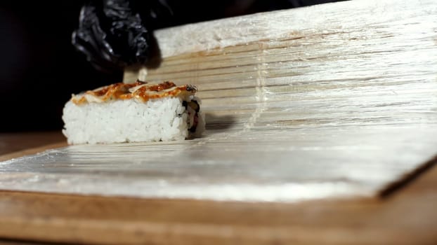 Close up view of chef in black cooking gloves rolling sushi with makisu, Japanese food preparation. Frame. Close up of hands rolling sushi with a traditional bamboo mat.