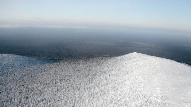 Calm and cold landscape with the endless valley of frozen forest. Clip. Aerial view of a snow covered mountain.
