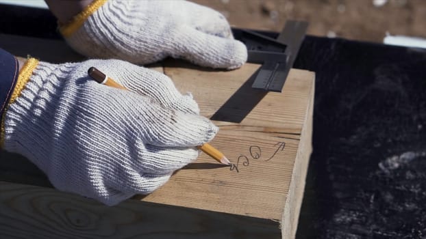 Close up for hands of a carpenter in protective gloves writing something on a wooden board. Clip. Joinery works, measuring and marking the wood, woodwork and furniture making concept.