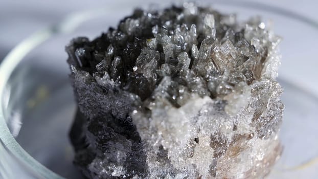 Beautiful unusual gray-black crystal stone cassiterite with a metallic sheen standing in the glass stand. Stock footage. Close up for shining crystal standing on the table.