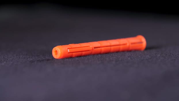 Close up of red plastic building dowel lying on the dark grey surface. Stock footage. Orange dowel, details of the construction of new housel.