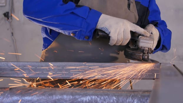 Craftsman sawing metal with disk grinder in workshop. Grinding metal with sparks flying. Electric wheel grinding on steel structure in factory Low speed shutter. Metal grinding with orange flying sparks.