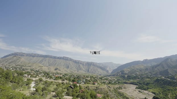 A drone flying over the mountains.Action. Beautiful daytime summer landscape with mountains and blue sky overhead, also with residential buildings and green trees.