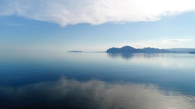 Stunning view from the meadow on calm dark blue water surface. Shot. Blue sky reflected in lake calm water.