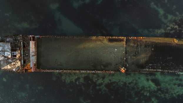Aerial top view for wrecked ship along the rocky coast in blue water. Shot. Old sunk boat near sea shore, view from above.
