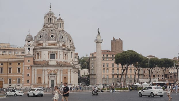 Italy, Rome - July 14, 2022: Lively city street with old buildings and Catholic church. Action. Tourists on road with cars on background of historic Catholic church. Church of St. Maria Loreto in Rome