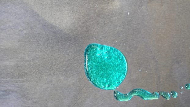 Top view of big turquoise stain on grey metal background holding stil. Big drop of bright teal paint with glowing particles on metal sheet surface.