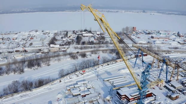 Industrial aerial background with the crane at the construction site. Clip. Winter frozen landscape, concept of heavy machinery.