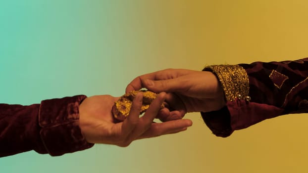 Close up for eastern man hand giving a big gold nugget to another man, isolated on green and yellow background. Stock. Eastern man paying by piece of gold ore, eastern bazar selling concept.