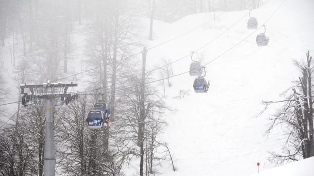 Winter ski resort with ski lifts on mountain. Ski slope with ski lifts and runs in foggy weather. Active holidays in winter