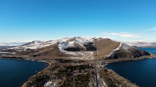 Aerial panoramic view of a large dark blue lake, blue sky, and mountains covered by snow. Footage. Picturesque natural valley.