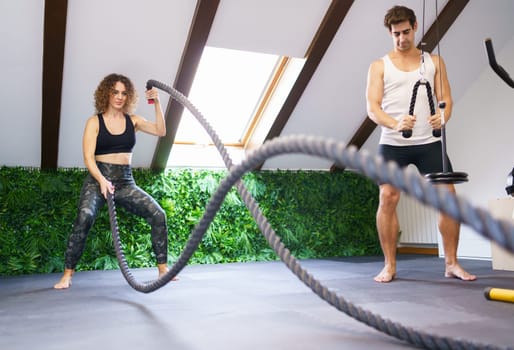 Strong sportswoman exercising with battle ropes during training
