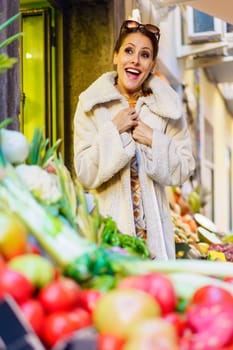 Smiling woman excited over assorted ripe fruits in shop at daylight