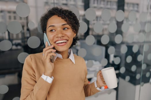 Positive female freelancer is talking phone with client while standing on coworking background