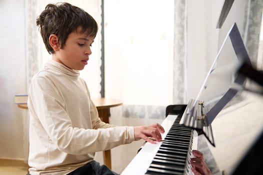 Adolescent boy performing classical composition, touching the keys and feeling rhythm while playing grand piano at home