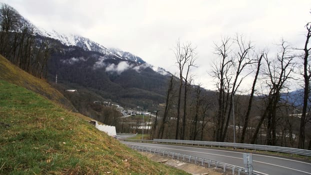 Breathtaking landscape of a mountain road and a moving car on cloudy background with snowy mountain. Mountain serpentine road with driving vehicle.