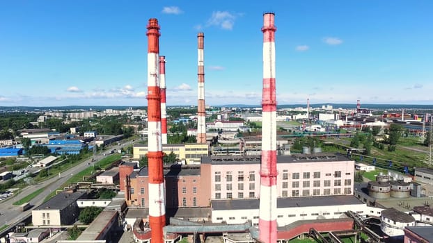 Aerial for factory chimneys and the cityscape in a summer, sunny day. Footage. Industrial zone in the city on blue, cloudy sky background.