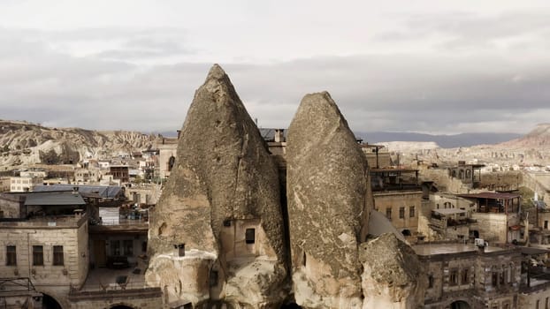 Ancient stone dwellings carved from tuff in Cappadocia, Turkey. Action. Aerial view of unusual beautiful nature, rock formations, city, and cloudy sky.