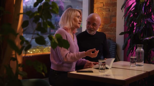 Elderly woman and man communicate in cafe. Stock footage. Beautiful elderly couple is having date in cafe. Evening date of elderly couple in cafe