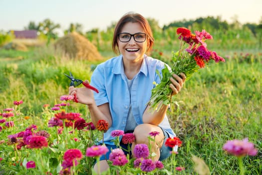 Smiling middle aged female holding bouquet of fresh zinnia flowers in garden