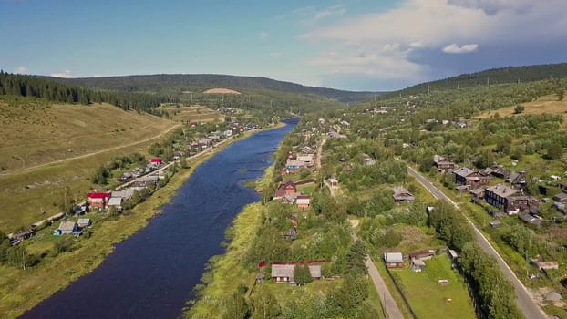 A view from a height of a small town with a river. Clip. Large houses with forests and trees against the blue sky.