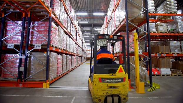 Poland, Warsaw- September 14, 2022: Stacker on large warehouse. Creative. Man in car for transportation of goods rides on skald. Rows of warehouse with goods and cargo and moving stacker