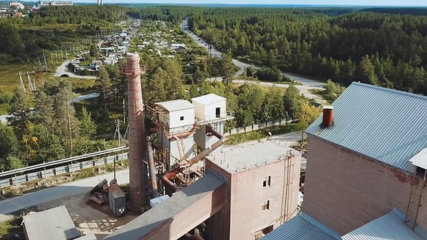 Factory with brick chimney on background of village. Stock footage. Top view of brick factory with chimney on background of town with green forest in summer
