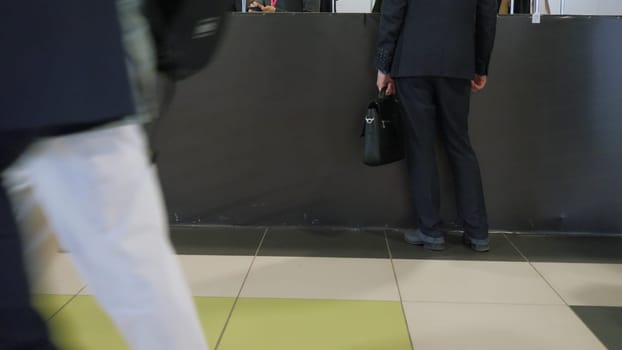 Businessman standing at window of service. Media. Legs of businessman standing at window of service or airport. Public place with crowds of people and businessman at reception