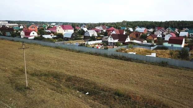 Aerial view of cottage village near the empty field for future building in the end of summer against blue cloudy sky. Beautiful countryside landscape
