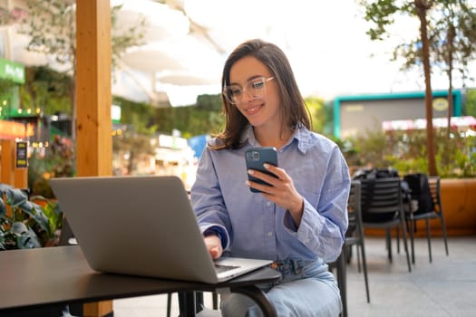 Freelance woman sitting in cafe working with laptop on terrace