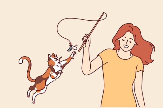 Woman plays with cat and waves bow on string, feeling pleasure thanks to presence of pet