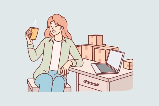 Woman small business owner drinks coffee sitting at table with boxes, takes short break