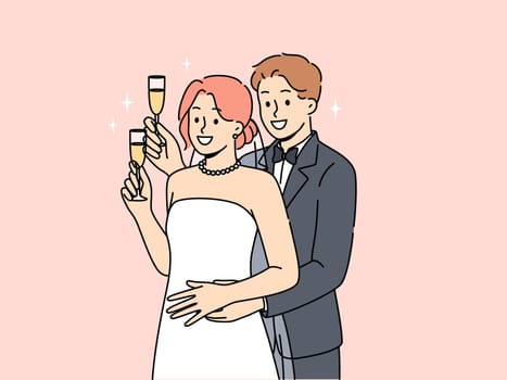 Newlywed man and woman stand in embrace and hold glasses of champagne during wedding ceremony