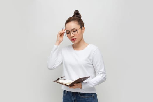 Intelligent asian lady in glasses taking notes, holding notepad and pen, standing over white
