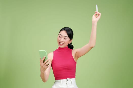 Smiling woman sitting on podium showing credit card and holding smartphone in another hand