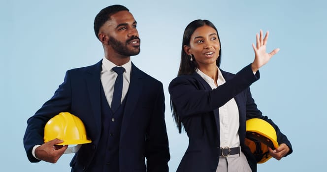 Business people, architect and planning in vision for building or construction against a blue studio background. Man and woman in engineering or project plan with hard hat for safety on mockup space
