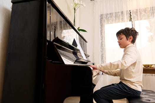 Adorable boy pianist, musician expressing positive emotions while enjoys playing grand piano at home. People and hobbies